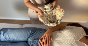 Fisioterapeuta a segurar um modelo anatómico da pélvis durante uma consulta, enquanto uma paciente relaxa deitada na marquesa
