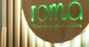 Logótipo iluminado com letras verdes sobre madeira, representando um espaço acolhedor e profissional especializado em cuidados maternos e infantis