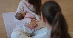 Mãe a amamentar o bebé numa sessão de apoio à amamentação, acompanhada por uma profissional especializada