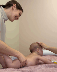 Sessão de osteopatia pediátrica com um bebé deitado numa marquesa, acompanhado por uma terapeuta sorridente.