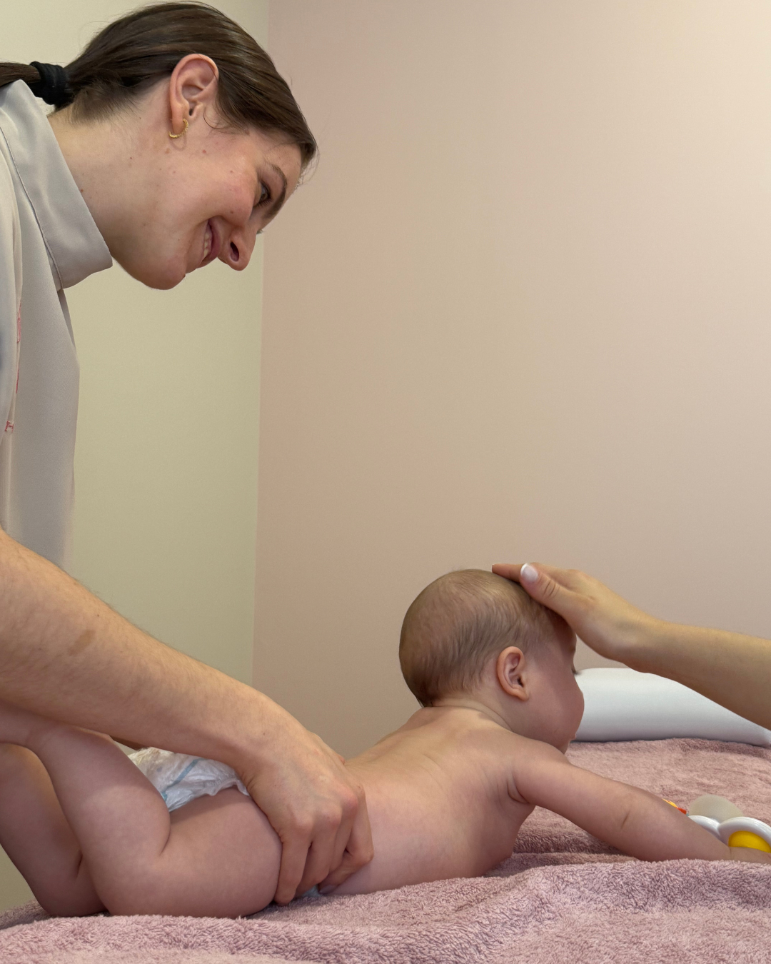 Sessão de osteopatia pediátrica com um bebé deitado numa marquesa, acompanhado por uma terapeuta sorridente.