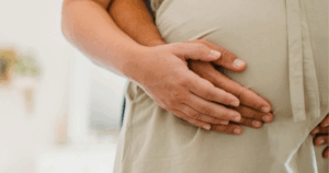 Casal grávido com as mãos unidas sobre a barriga num gesto de apoio mútuo