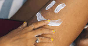 Mulher aplica creme nas pernas com um desenho de sorriso feito com loção