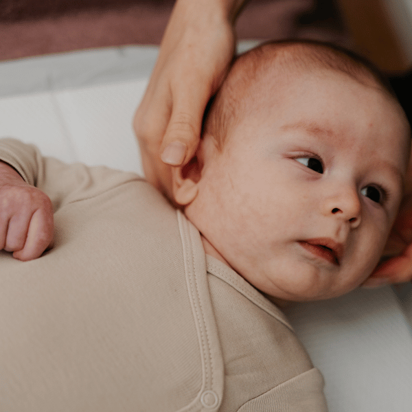 Bebé deitado durante uma consulta de osteopatia pediátrica, enquanto a profissional posiciona suavemente as mãos junto à cabeça e ao pescoço.